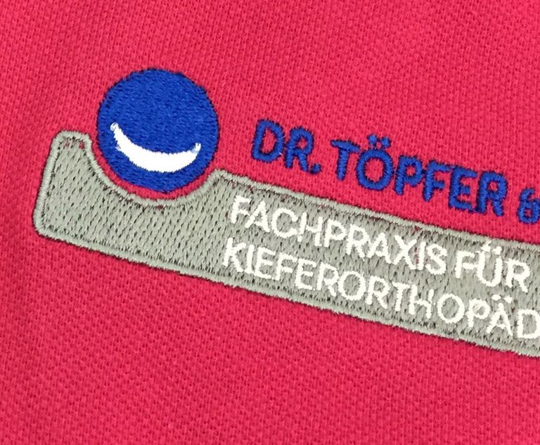 Detailaufnahme der Logo-Stickerei von 'Dr. Töpfer & Kollegen Fachpraxis für Kieferorthopädie Hanau'