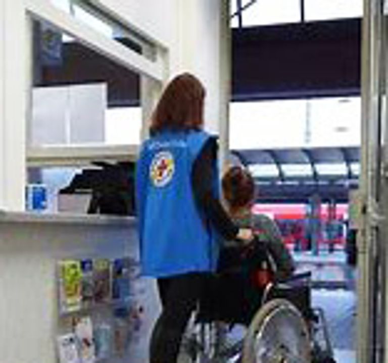 Mitarbeiterin der Bahnhofsmission schiebt einen Rollstuhlfahrer